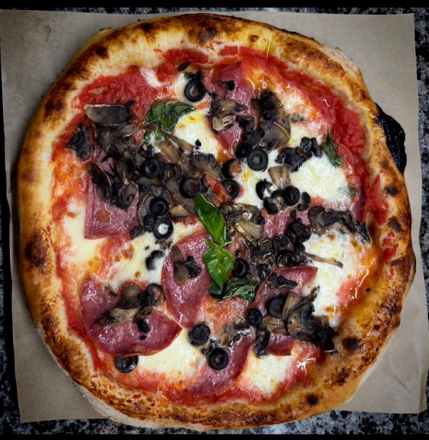 A blistered, fresh-baked pizza with salami, olives, mushrooms and basil at Neama